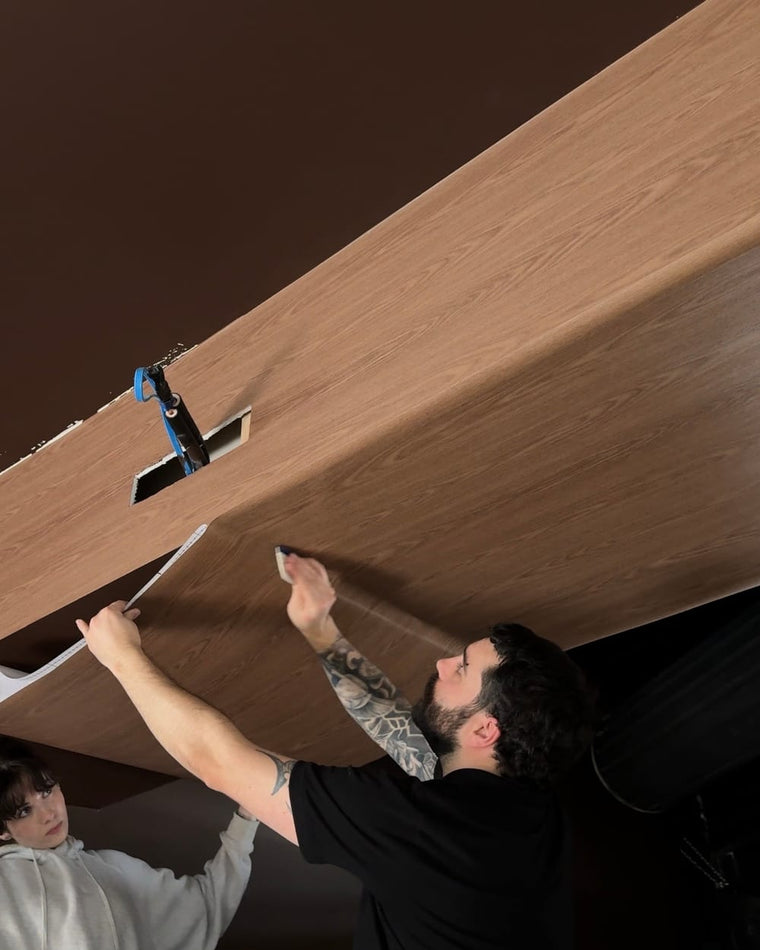 Two installers smoothing a sheet of Maison Walnut wrap onto an angled panel at The Feel Good Hood
