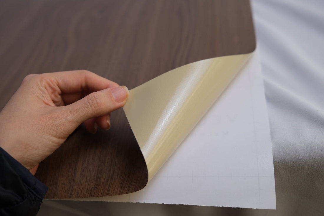 A hand lifting a dark walnut wrap sheet away from its backing on a cabinet surface