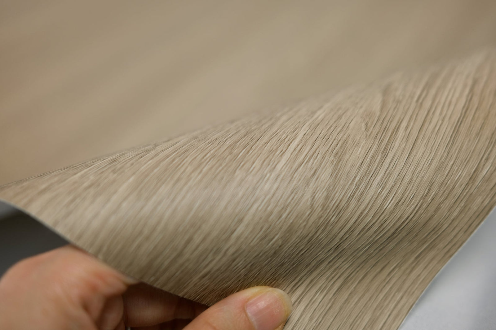 A hand bending a flexible light oak wrap sheet to show the edge and film