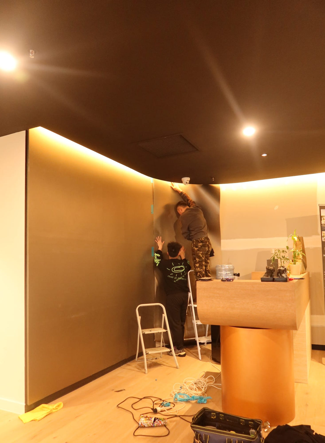 Installers applying dark Meteorite vinyl wrap to the curved reception wall at VICPROP, with the timber reception desk in the foreground