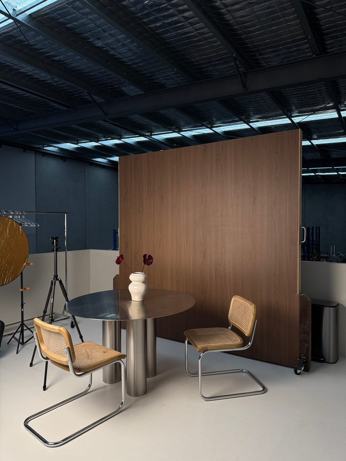 Natural Walnut warm brown wood-grain backdrop wall in an editorial studio, with a table and chairs in front