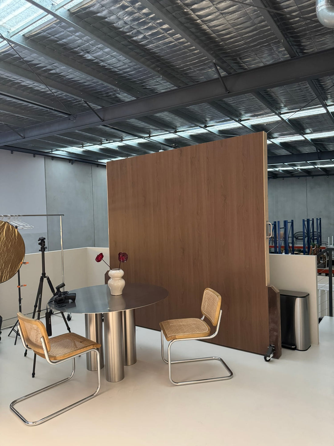 Natural Walnut wood-grain backdrop wall viewed from the side, showing the studio seating area and exposed ceiling