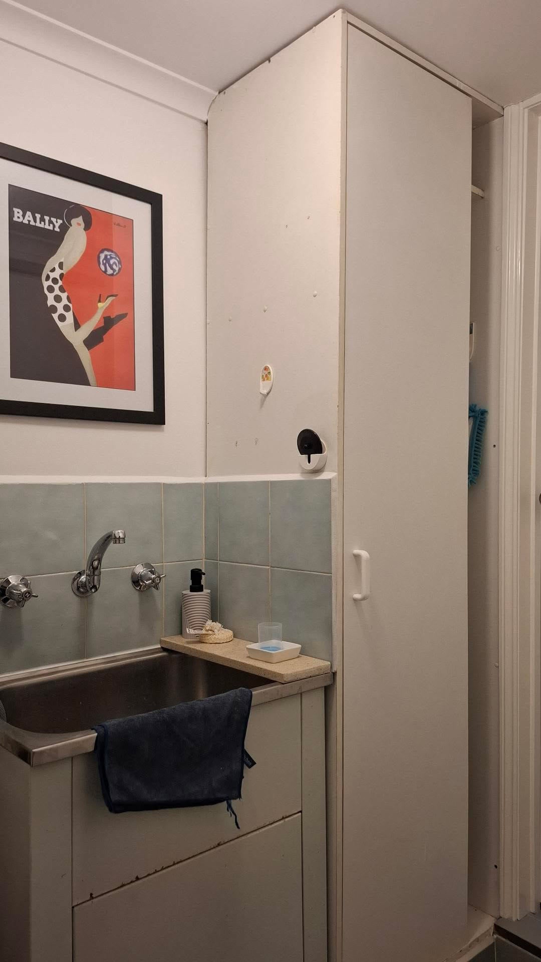 The same laundry cupboard before wrapping, plain white and marked, beside a stainless laundry tub